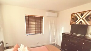 Un dormitorio con cama, cómoda, televisor y ventana con persianas.