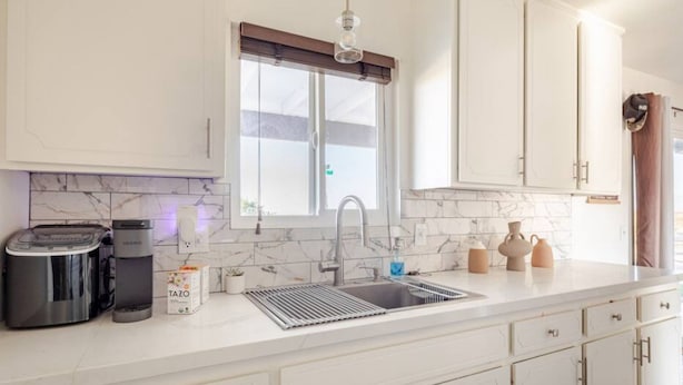 Una cocina moderna con armarios blancos, un lavamanos de acero inoxidable, una cafetera y un hervidor.
