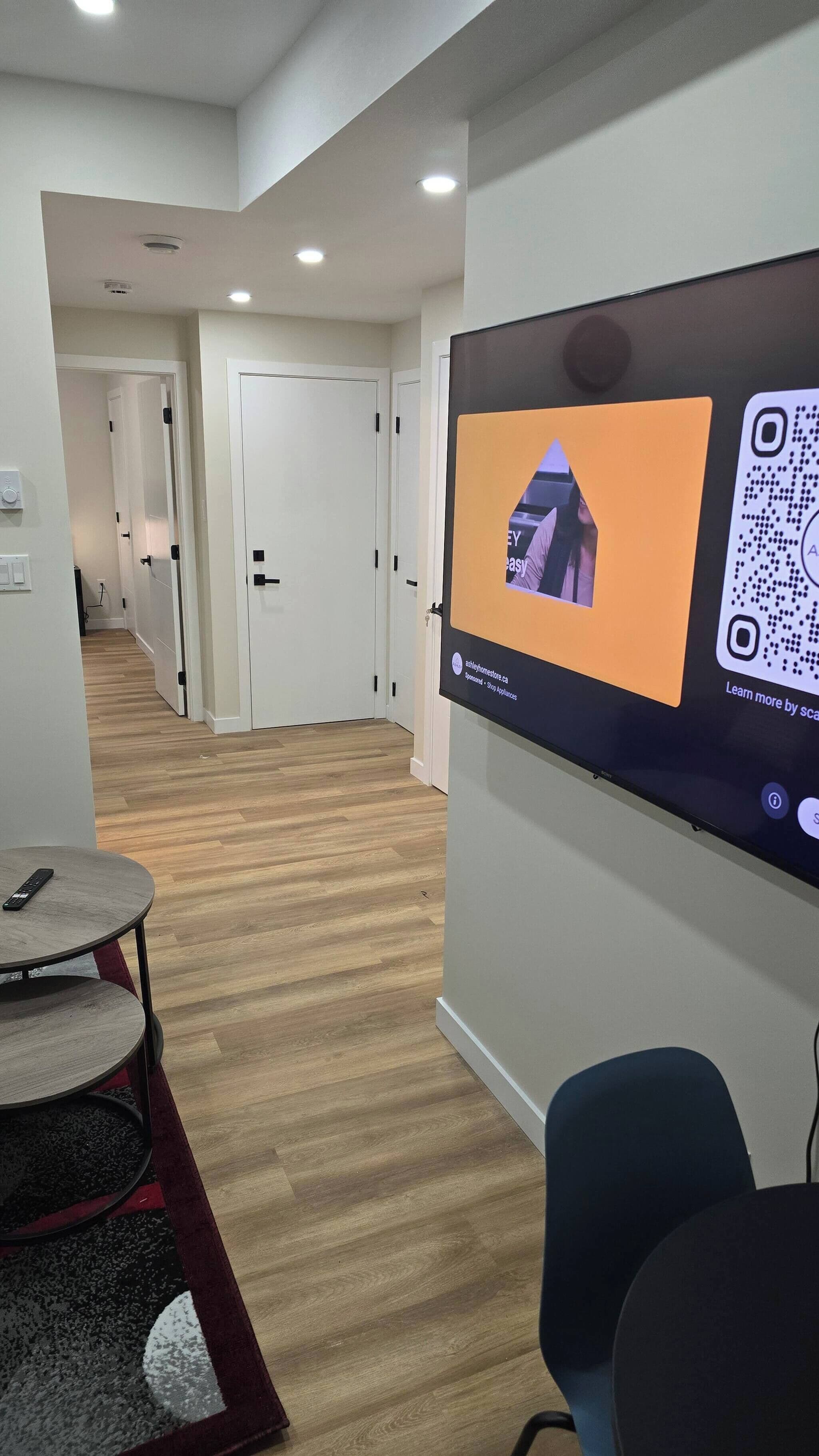 A modern interior with a flat-screen TV displaying a QR code and a remote control on a round table.