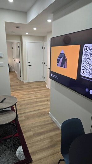 Un interior moderno con un televisor de pantalla plana mostrando un código QR y un control remoto sobre una mesa redonda.