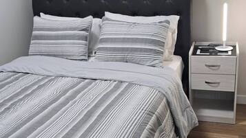 A bedroom with a tufted headboard, striped bedding, a bedside table with drawers, and a nightstand with a lamp.