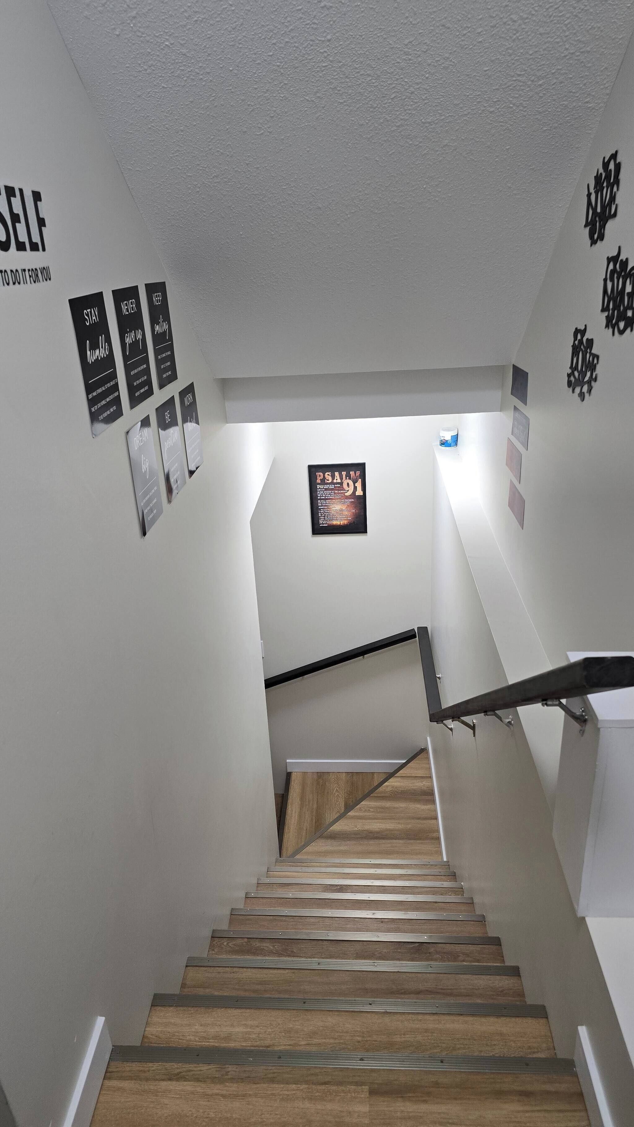 A staircase with wooden steps and metal handrails, leading to a landing with a framed inspirational quote.