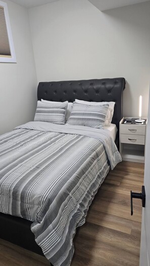 Una cama bien hecha con ropa de cama a rayas, un cabecero tapizado oscuro y una mesita de noche con una lámpara.