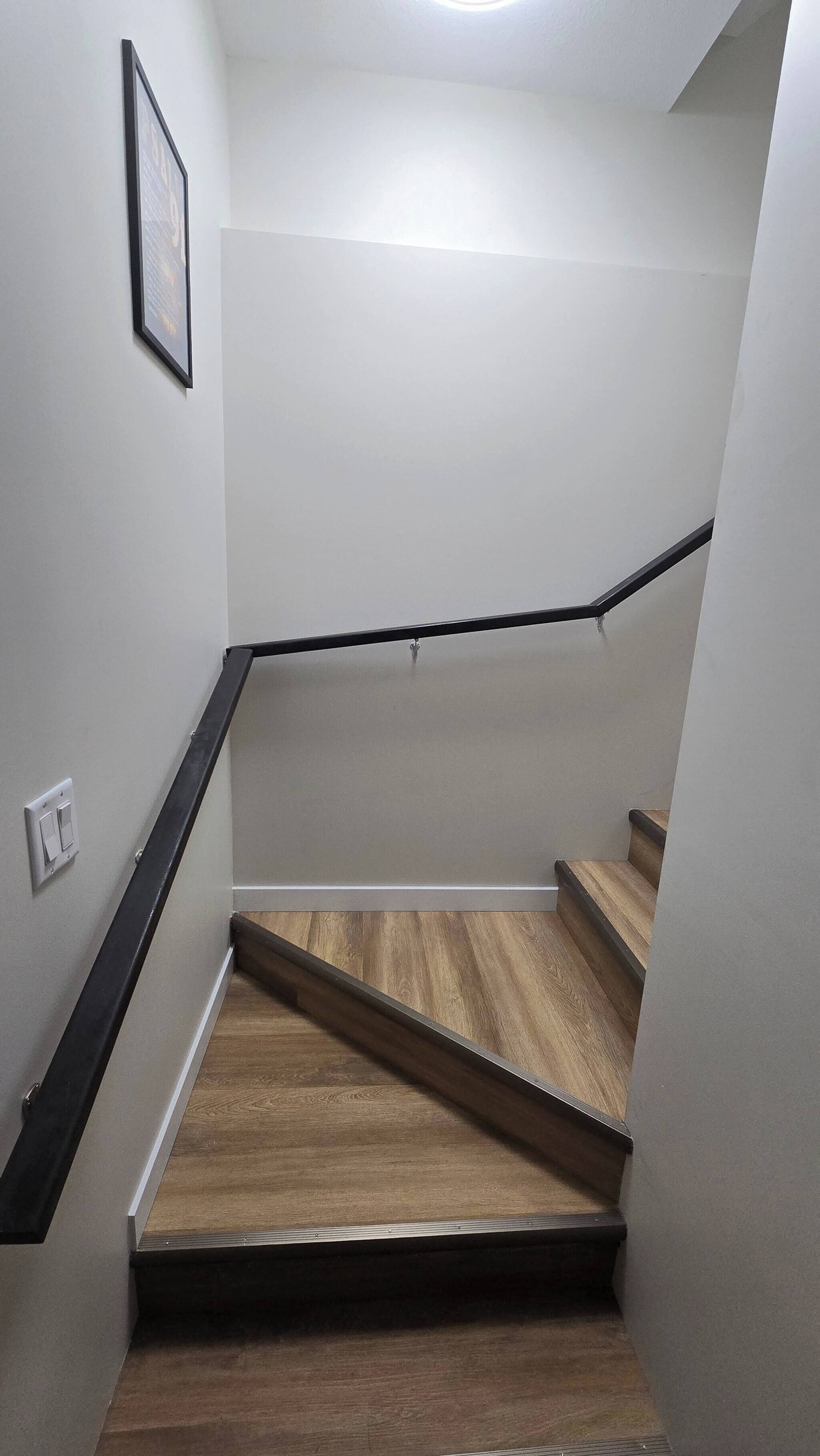 Un escalier avec des marches en bois et des rampes noires, menant à un palier où se trouve un luminaire.