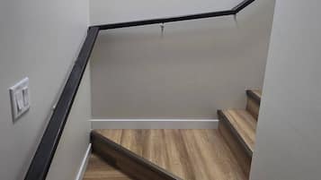 Un escalier avec des marches en bois et des rampes noires, menant à un palier où se trouve un luminaire.
