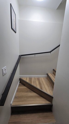A staircase with wooden steps and black handrails, leading to a landing with a light fixture.