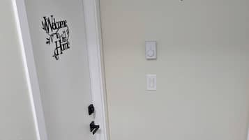A hallway with a white door, a 'Welcome to Our Home' sign, a 'hello' doormat, a thermostat, and a white radiator.
