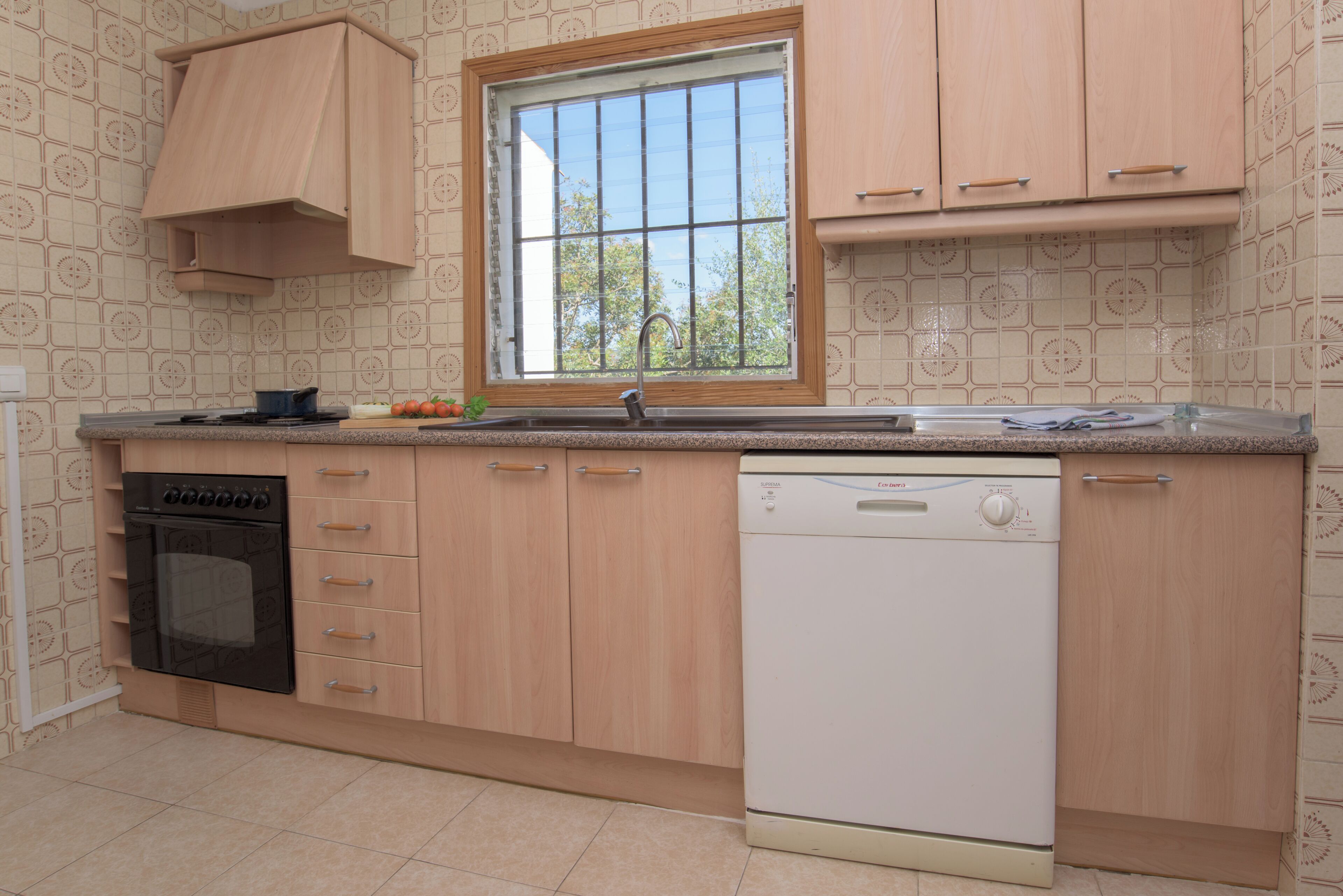 Eine Küche mit Holzausstattung, Backofen, Geschirrspüler und einem Fenster mit Blick auf Bäume.