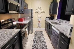 A kitchen with stainless steel appliances, a red toaster, and a decorative backsplash. - Delightfully Villainous (Four Corners)