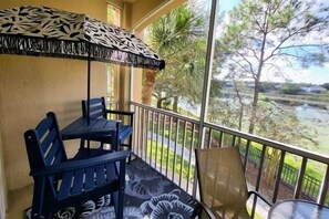 Ein Balkon mit Tisch und Stühlen, der auf ein Gewässer und viel Grün blickt.