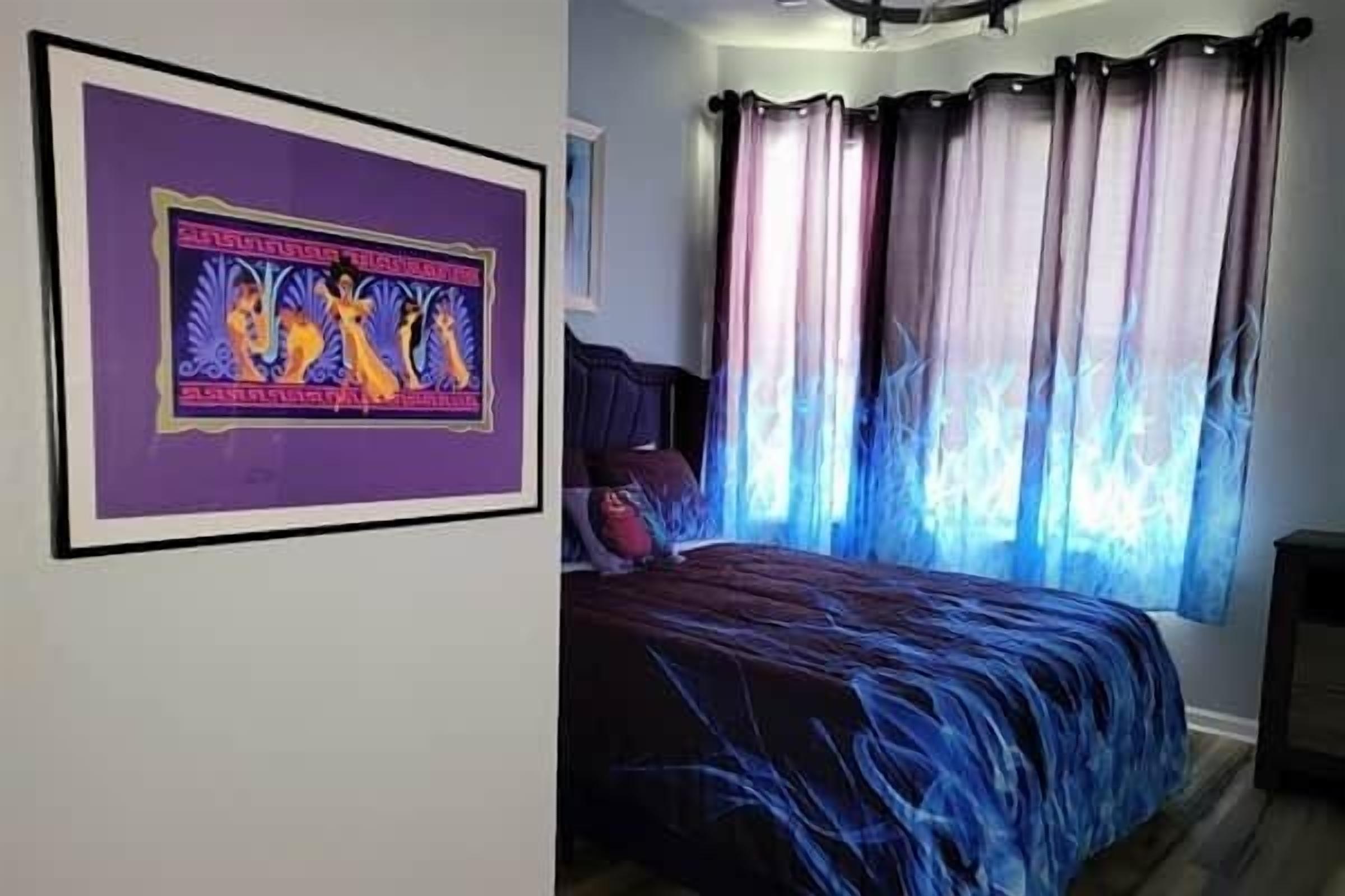 A bedroom with a bed, curtains, and a framed picture on the wall.