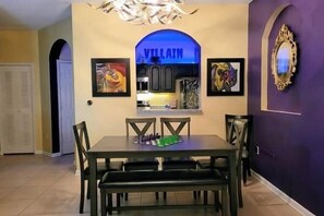 A dining area with a table and chairs, a chandelier, and framed artwork on the walls. - Delightfully Villainous (Four Corners)