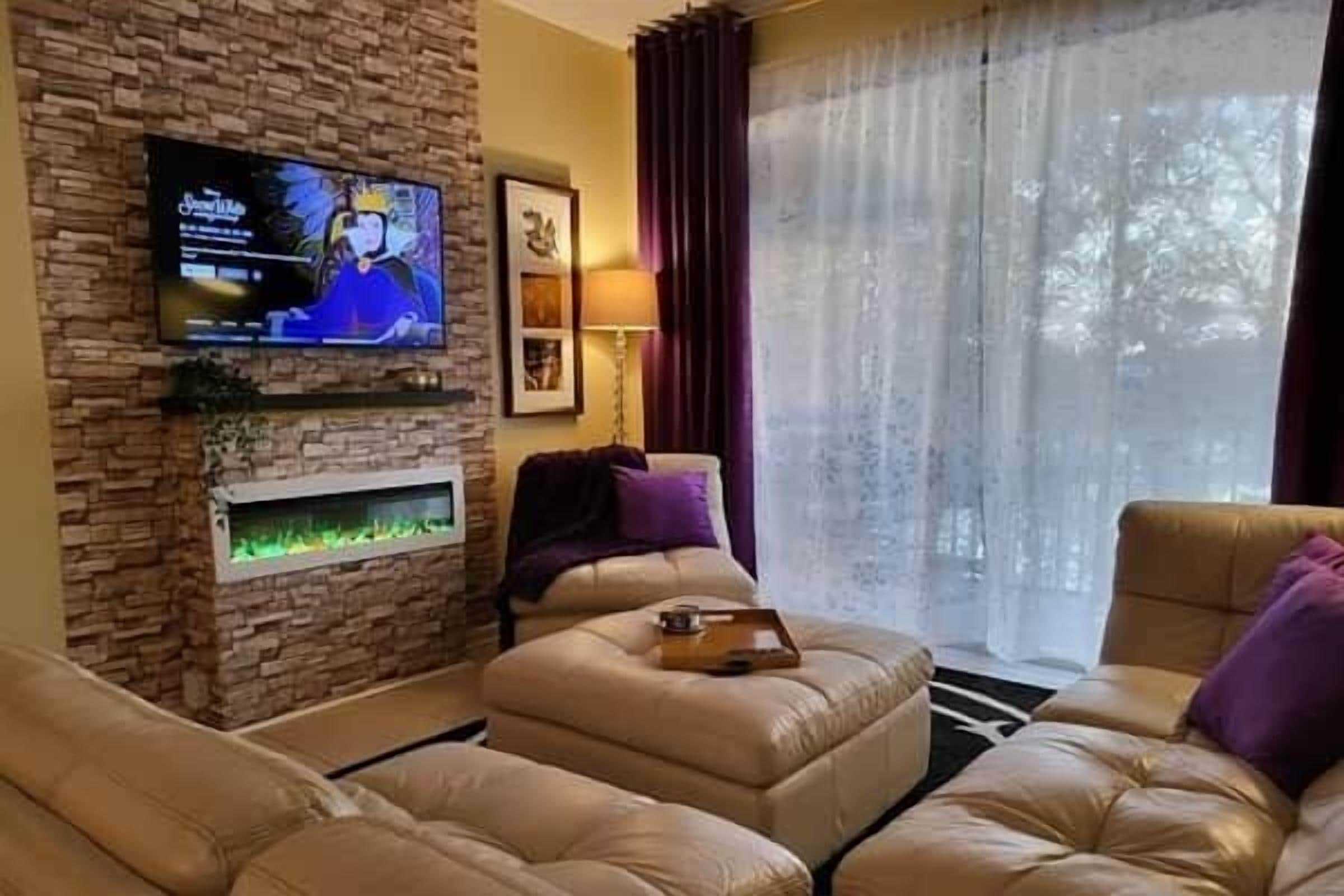 Un salon avec un mur en pierre, un téléviseur à écran plat, une cheminée et une grande fenêtre avec des rideaux.