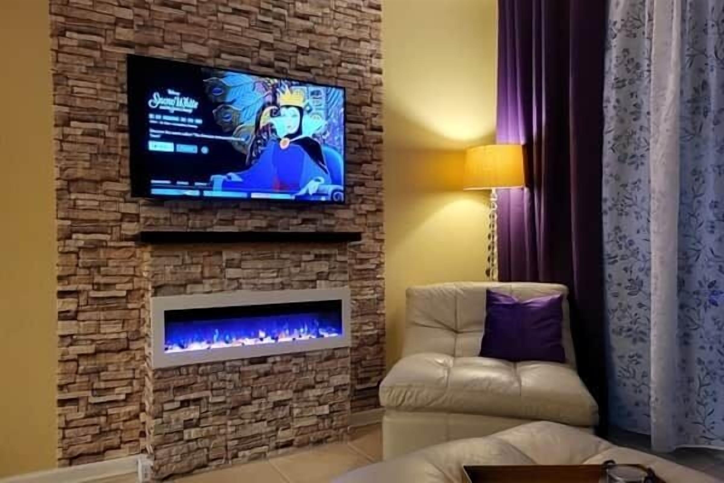 Una sala de estar con una pared de piedra, un televisor de pantalla plana montado sobre una chimenea, un sofá de cuero y una cortina estampada.