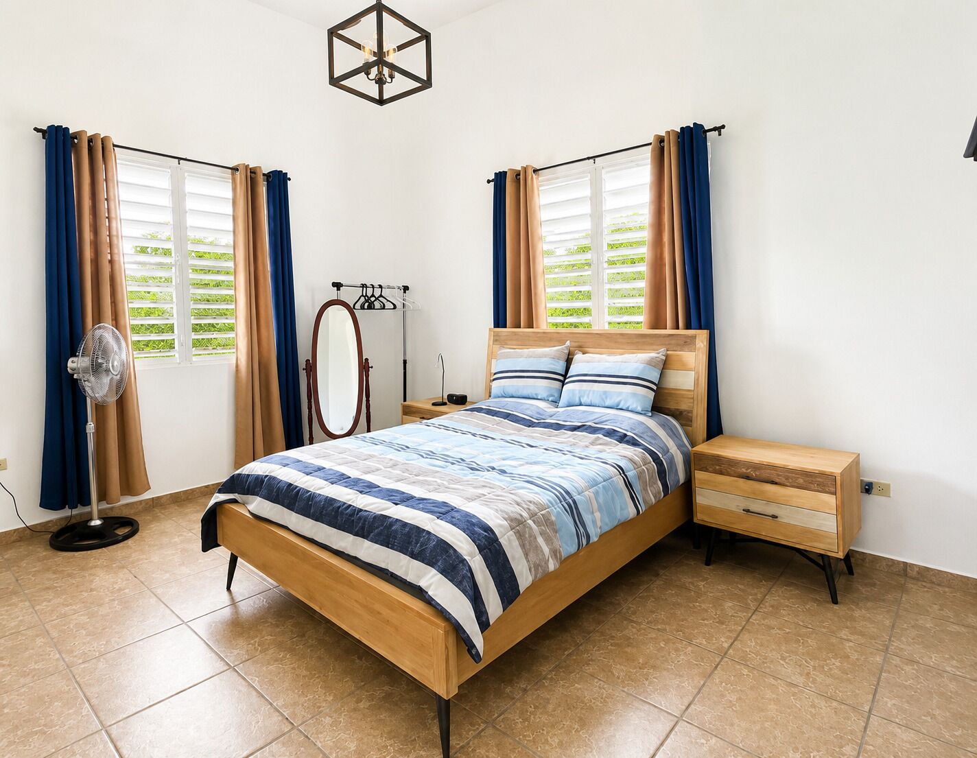 A bedroom with a bed, bedside tables, a mirror, and a fan.
