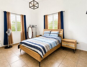 A bedroom with a bed, bedside tables, a mirror, and a fan.