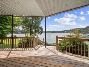 Eine Holzterrasse mit Geländer, die auf einen See mit umgebendem Grün und Bäumen blickt.