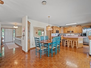 A spacious kitchen with wooden cabinets, a central island, and a dining area with blue chairs. - Decked Out in Dismal - Decks and Amenities! (Arley)