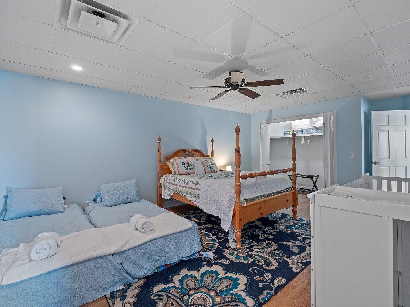 Une chambre à coucher avec un lit à baldaquin, un lit simple, un berceau et un ventilateur de plafond.