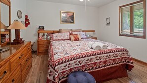 Ein Schlafzimmer mit einem Bett, einer Kommode, einem Spiegel, einem Deckenventilator, einem Fenster mit Jalousien und einem gerahmten Bild an der Wand.