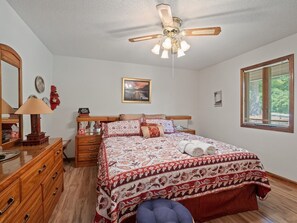 Ein Schlafzimmer mit einem Bett, einer Kommode, einem Spiegel, einem Deckenventilator, einem Fenster mit Jalousien und einem gerahmten Bild an der Wand.