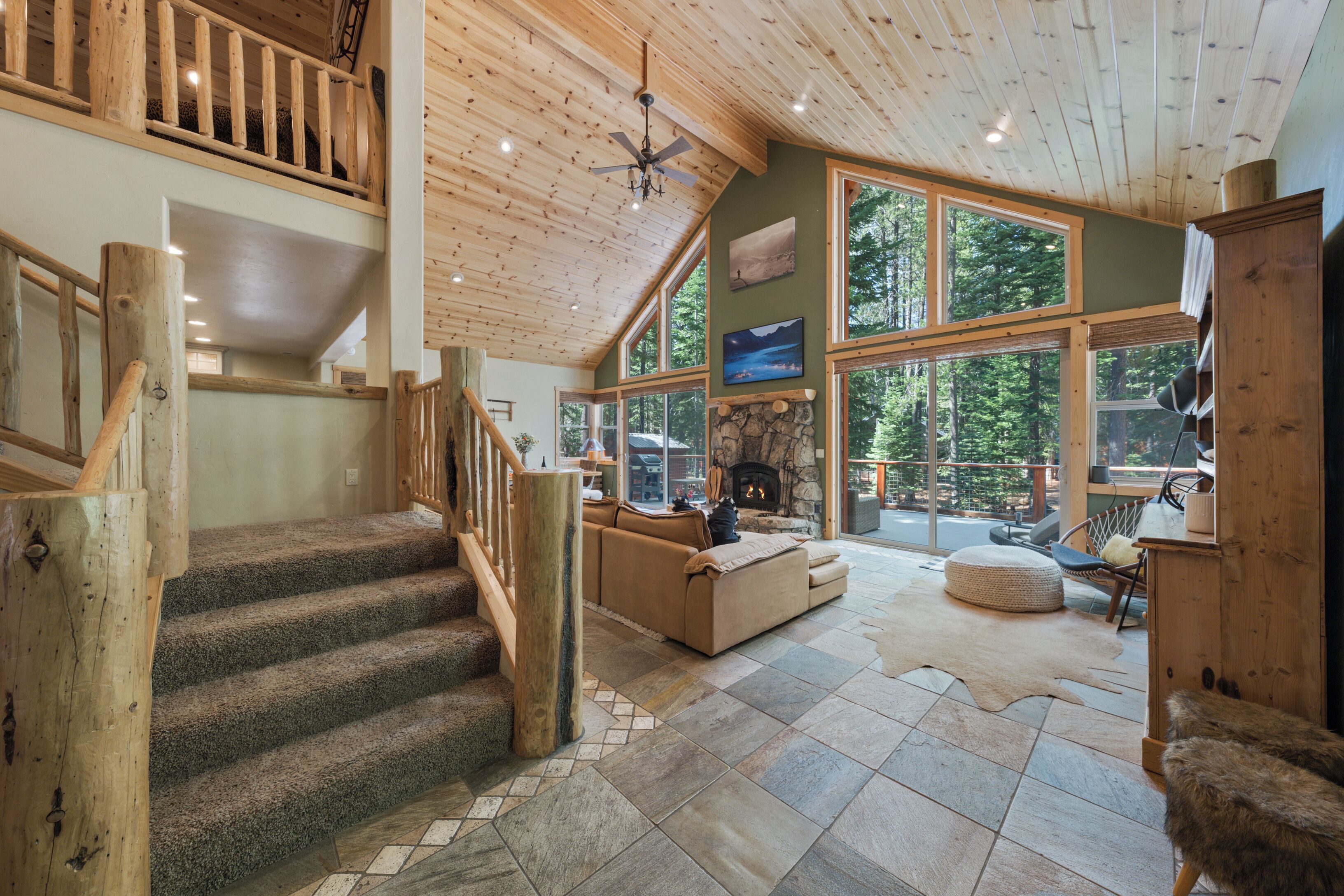 Un intérieur spacieux avec une cheminée en pierre, une grande fenêtre donnant sur une forêt et un escalier en bois.