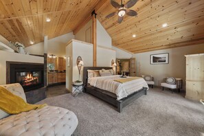 Ein Schlafzimmer mit Kamin, einem Bett, einem Deckenventilator und Blick auf die Küche.