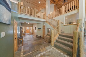 A spacious interior with a wooden staircase, a hallway leading to a door, and a dining area. - Tahoe Family Lodge | King Suite | Game Loft | Rec Center Access | Near Trails (Truckee)
