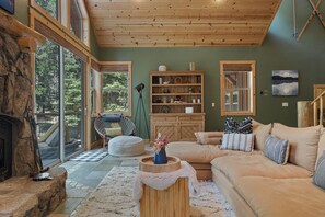 A spacious living room with a stone fireplace, a large window, and a cozy seating area. - Tahoe Family Lodge | King Suite | Game Loft | Rec Center Access | Near Trails (Truckee)