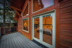 A wooden cabin with a deck, large windows, and a visible bedroom with a bed and nightstand. - Tahoe Family Lodge | King Suite | Game Loft | Rec Center Access | Near Trails (Truckee)