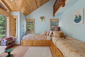 Ein Schlafzimmer mit zwei Holzbett, einem Fenster, einem Teddybär und einem Bücherregal.