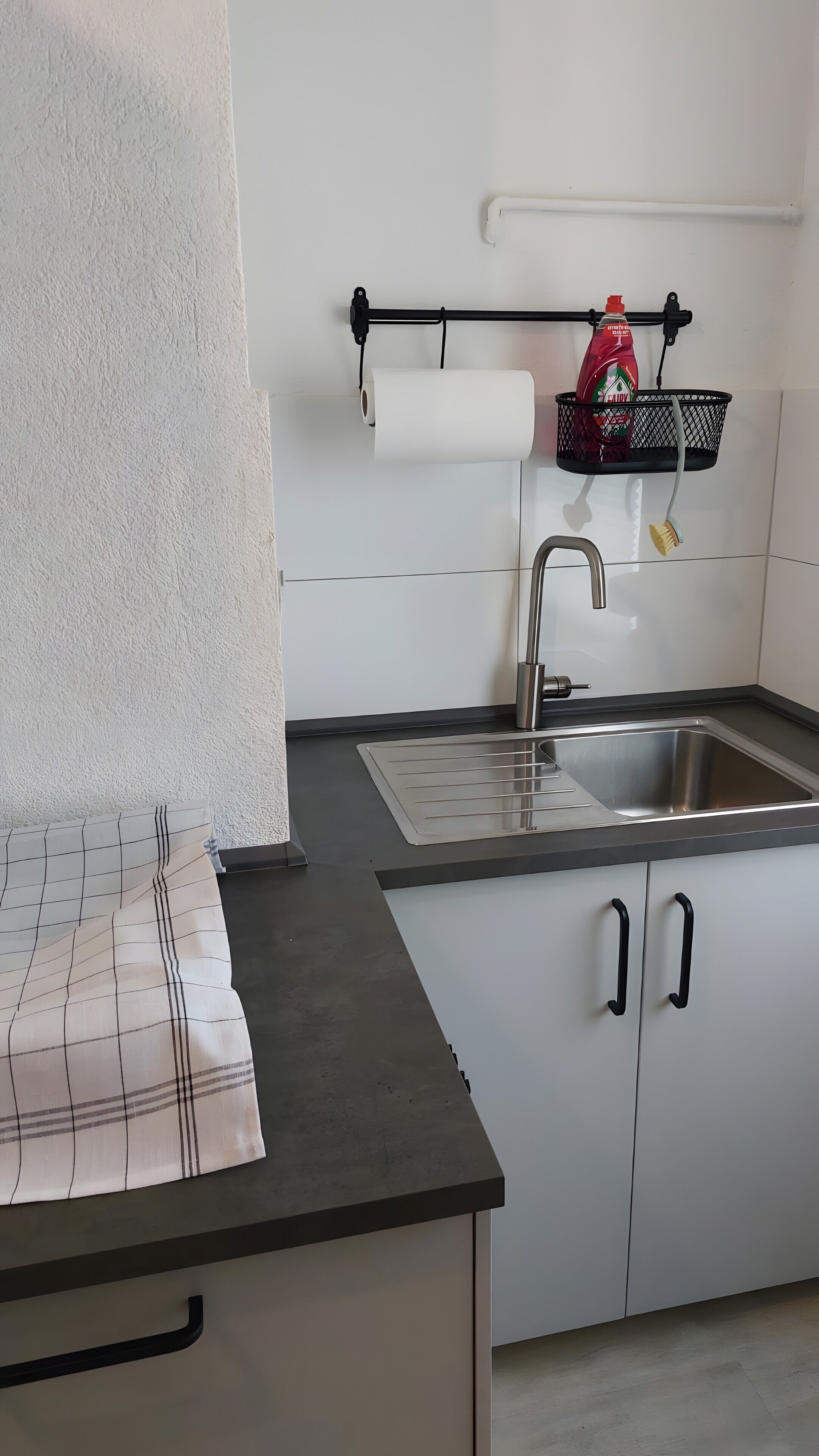 A kitchen with a stainless steel sink, white cabinets, a black countertop, and a roll of paper towels on a holder.