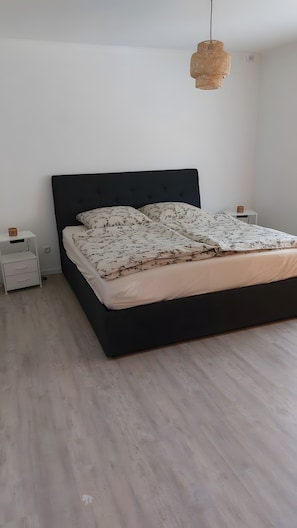 A bedroom with a black bed, white nightstands, and a woven light fixture.
