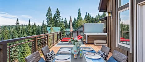 A deck with a table set for two, surrounded by wicker chairs, overlooking a forest.