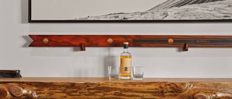 Una barra de madera con una botella y vasos, un cuadro con una pista de esquí, y un estante de madera con una etiqueta.