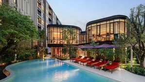 Un hotel moderno con piscina, sillas de lounge rojas y un edificio de vidrio.