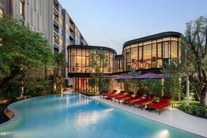 Ein modernes Hotel mit Schwimmbad, roten Liegestühlen und einem gläsernen Gebäude.