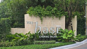 Letrero que dice 'The Base Cherng Talay', con un muro de piedra y follaje.