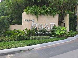Schild für 'The Base Cherng Talay' mit einer Steinmauer und Grünpflanzen.