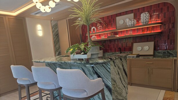Una cocina moderna con una isla de mármol, taburetes de bar, una planta en maceta y un salpicadero rojo.