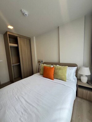 A hotel room with a bed, a nightstand, a lamp, a wardrobe, and a ceiling-mounted smoke detector. - Pet-Friendly Phuket Apartment | Pool & Gym (Cherngtalay)