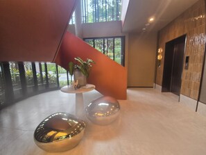 Eine moderne Lobby mit einem zentralen Tisch, zwei runden Sitzbereichen und einer Treppe mit rotem Akzent.