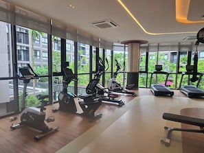 Ein modernes Fitnessstudio mit unterschiedlichen Trainingsgeräten, großen Fenstern und Blick auf Grünflächen.