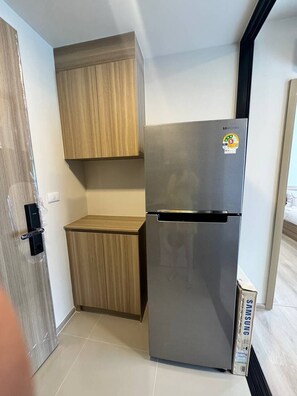 A compact kitchen with a stainless steel refrigerator, wooden cabinets, and a tiled floor. - Pet-Friendly Phuket Apartment | Pool & Gym (Cherngtalay)