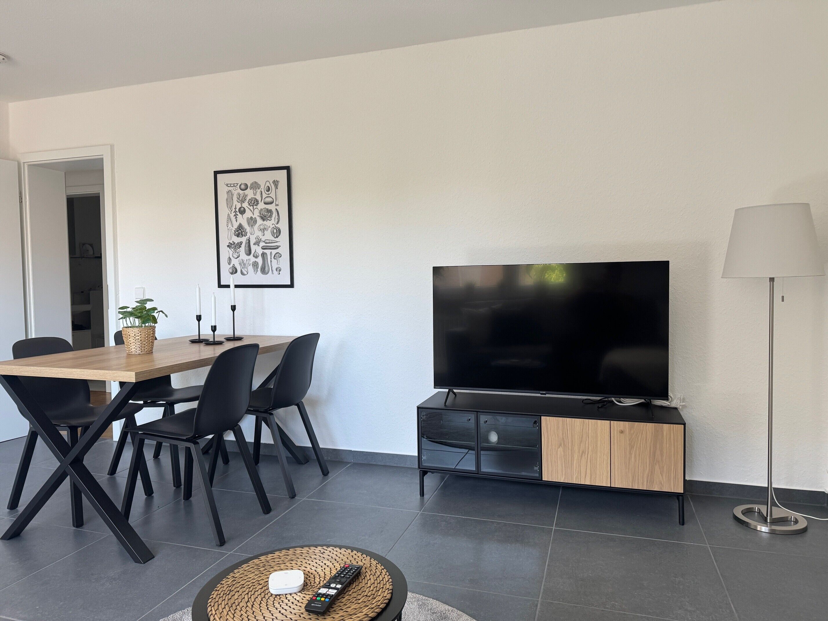 En moderne stue med et fladskærms TV, et spisebord med stole, en gulvlampe og et billede i ramme på væggen.