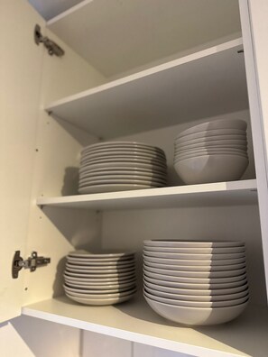 Eine Küchenschrank mit weißen Regalen, voll mit gestapelten weißen Tellern und Schüsseln.