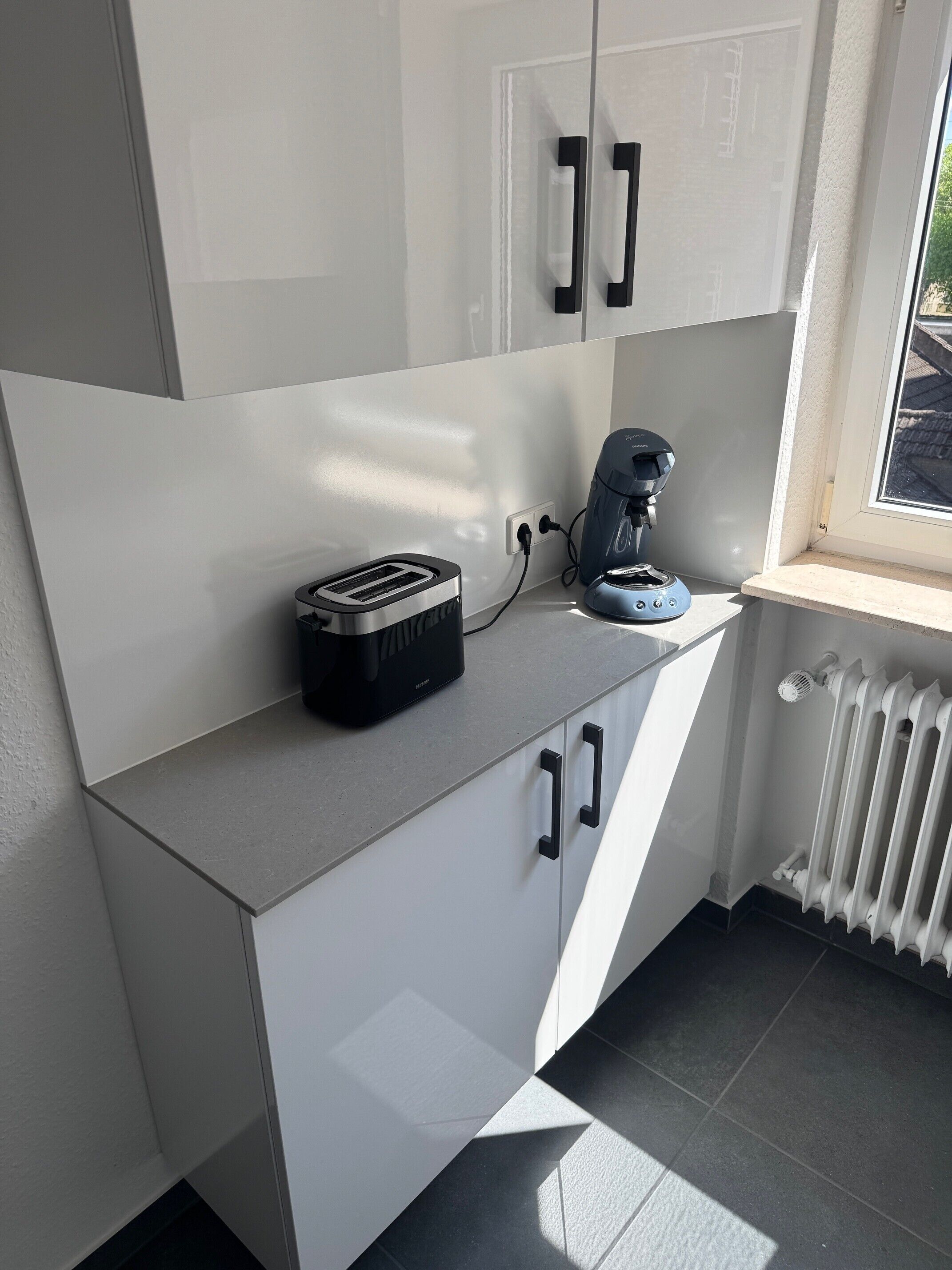 A modern kitchen with white cabinetry, a toaster, a coffee maker, and a window with a view.