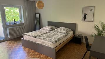 Une chambre à coucher avec un lit, un radiateur, une fenêtre avec des rideaux, un luminaire suspendu, un tableau encadré au mur et une plante.