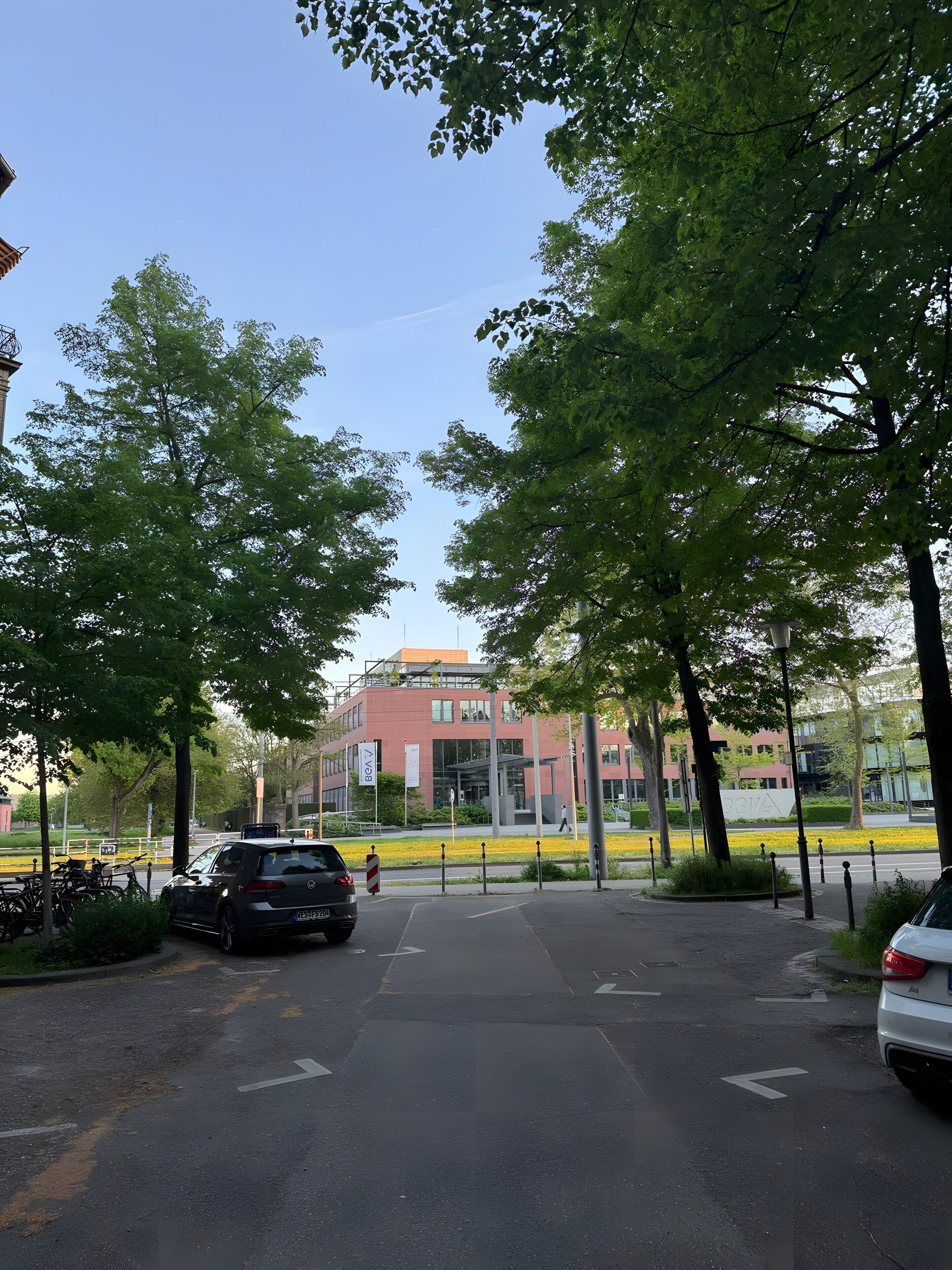 Un espace de stationnement avec des voitures, des arbres et un bâtiment à la façade rouge.