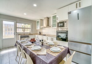 A modern kitchen with a dining table set for four, equipped with a refrigerator, oven, and microwave. - House with garden Can Nofre in Playa de Muro (Muro)
